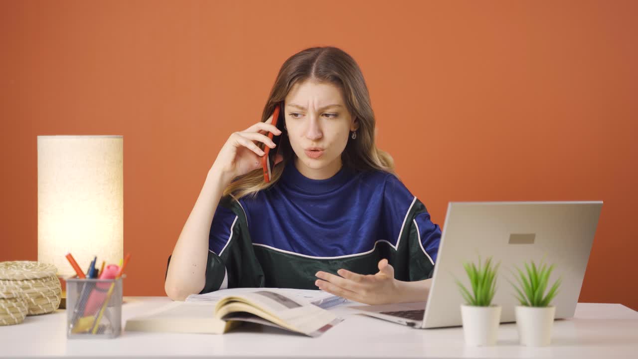 노트북을 사용하는 젊은 여성이 긴장해서 전화로 이야기하고 있습니다.