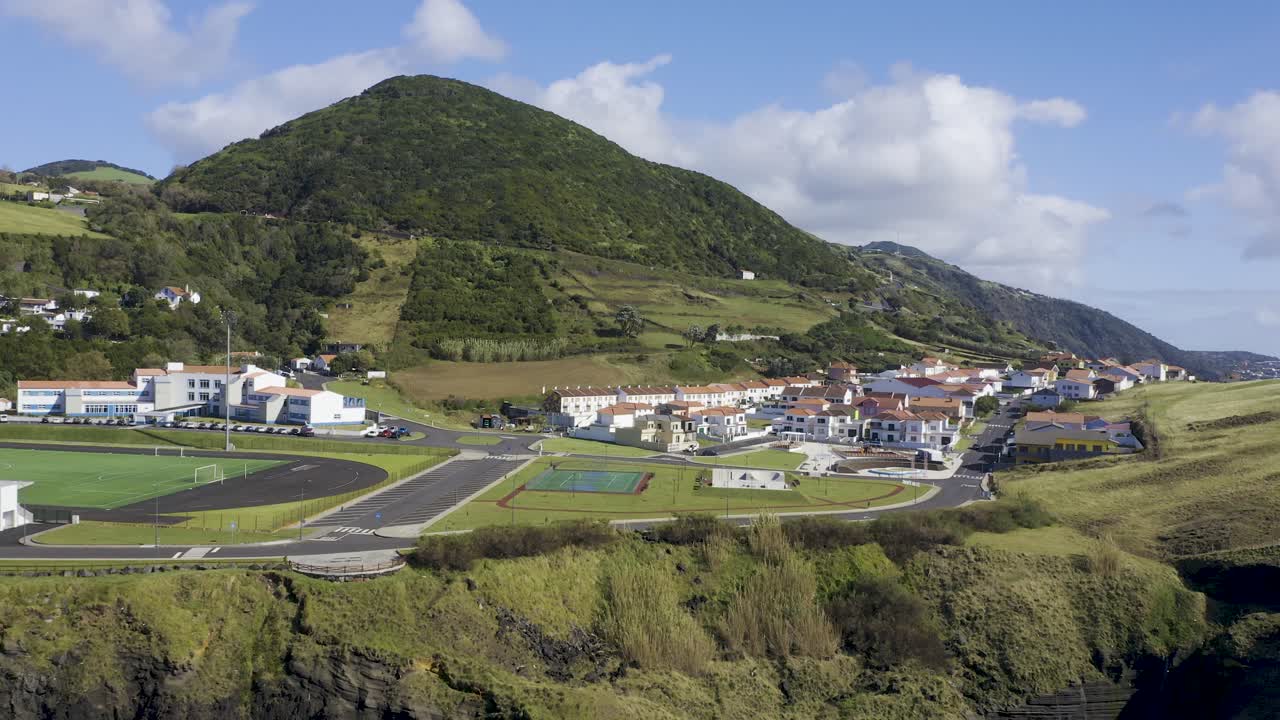 벨라스, 상 호르헤 섬, 아조레스, 백색 주택, 스케이트 공원, 운동장이 있는 마을의 포르투갈 조감도, 주변 산과 초목 돌리 카메라 무브먼트 드론 영상