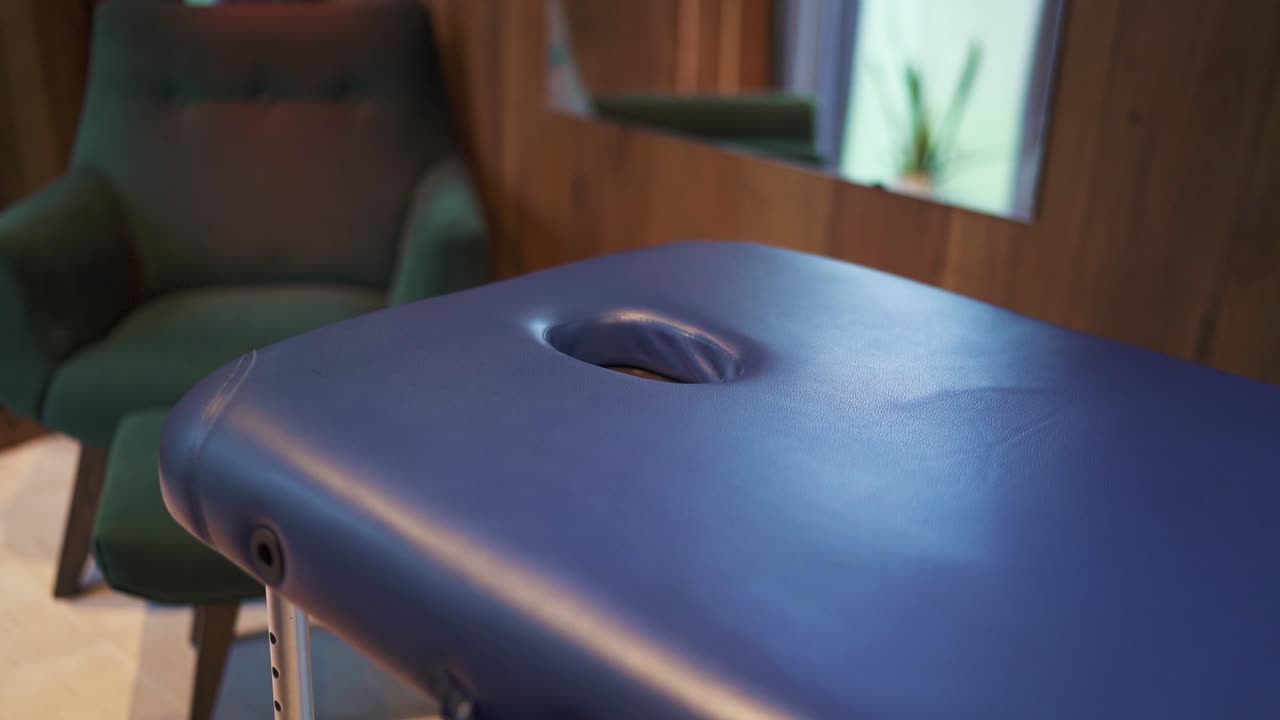 moderno centro de bienestar que ofrece terapia de masaje relajante con mesa de masaje vacía que muestra el agujero de la cara y el fondo borroso con un cómodo sillón y muebles de madera