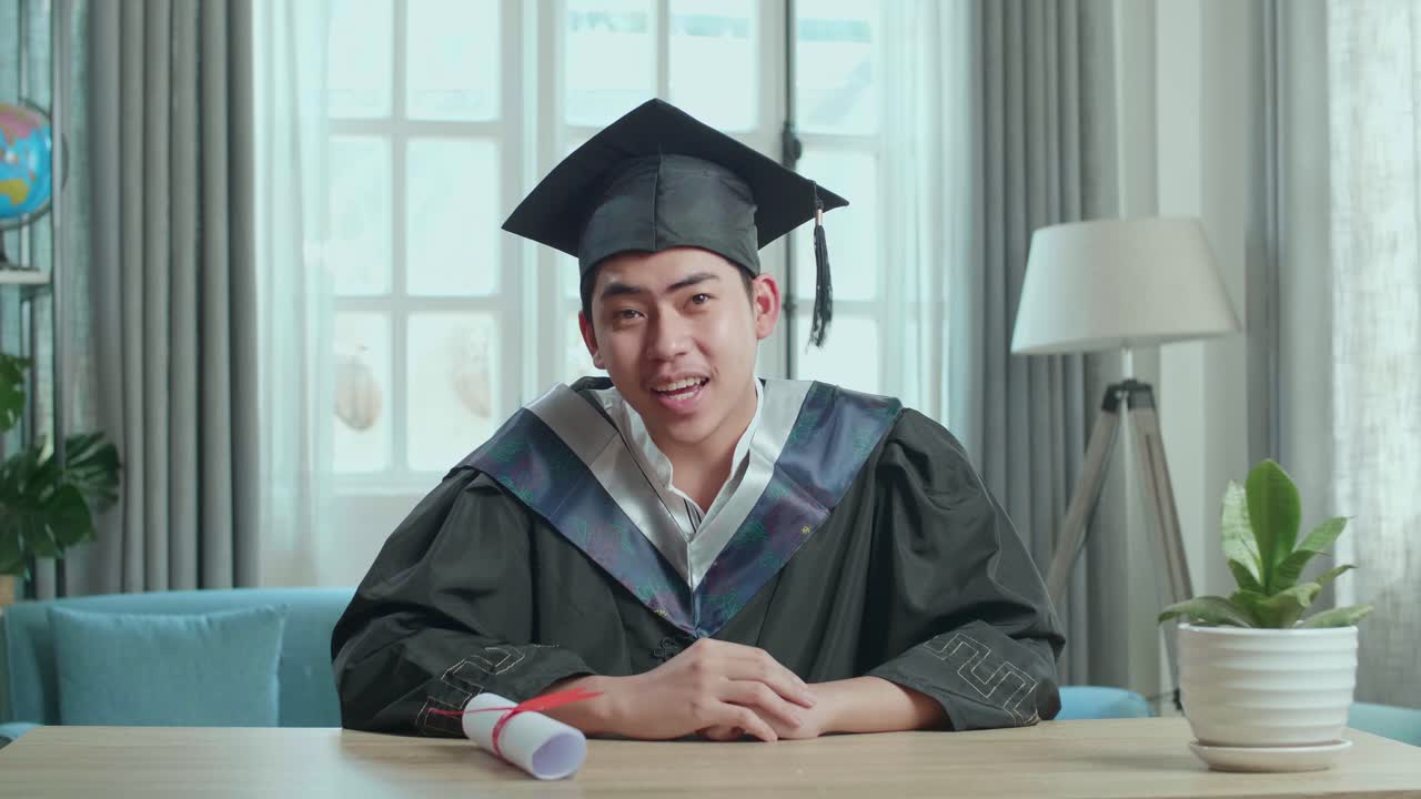 卒業式のドレスとキャップを着たアジア人男性がリビングでビデオコールをしている