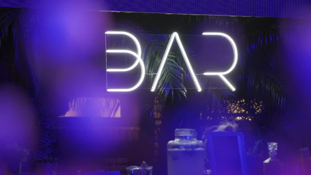 A neon sign for a bar with a blue background. The sign is lit up and has a white lettering