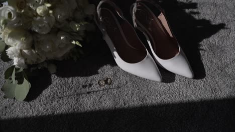 white bridal shoes and bouquet on a carpet with wedding rings in soft sunlight.