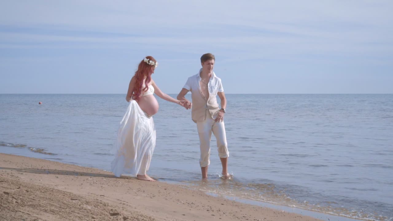해변에서 즐거움을 즐기는 사랑의 커플. 임신한 커플이 물을 뿌리고 있습니다.