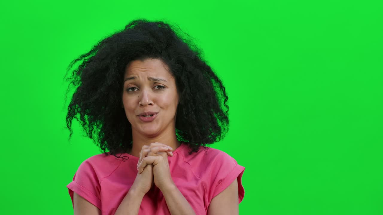 Portrait of young female African American keeping palm together and asking for something. Black woman with curly hair poses on green screen in the studio. Close up. Slow motion ready 59.97fps