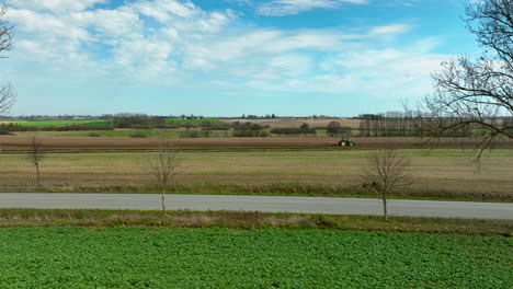 aerial view of a tractor working in the fields, with a lone tree in the foreground under a clear blue sky