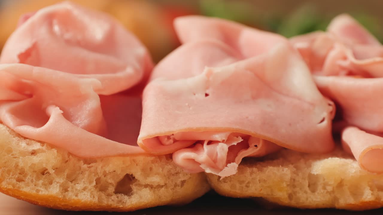 Mortadella ham sandwich, Traditional italian focaccia filled with thin pesto slices of mortadella, served by chef man in cafe restaurant. Macro of traditional italian spanish tapas antipasti.