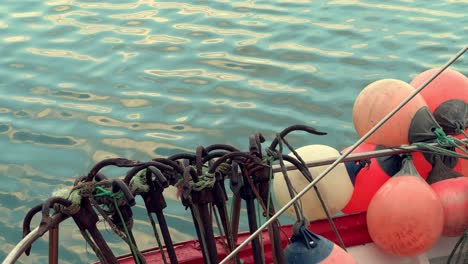 Shot-of-vibrant-colors-buoys-affixed-to-a-ship's-hull-has-a-background-of-sea-water-surface,-suspended-just-at-the-waterline,-metal-anchors,-evoking-themes-of-fishing-and-maritime-activities