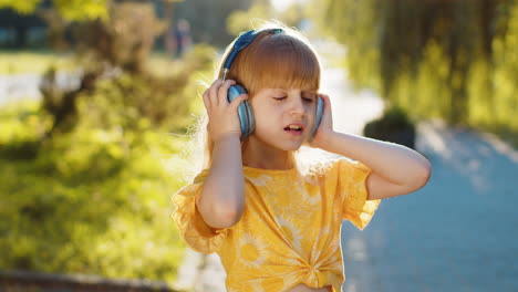 Happy-child-girl-in-wireless-headphones-choosing,-listening-music-in-smartphone-dancing-outdoors