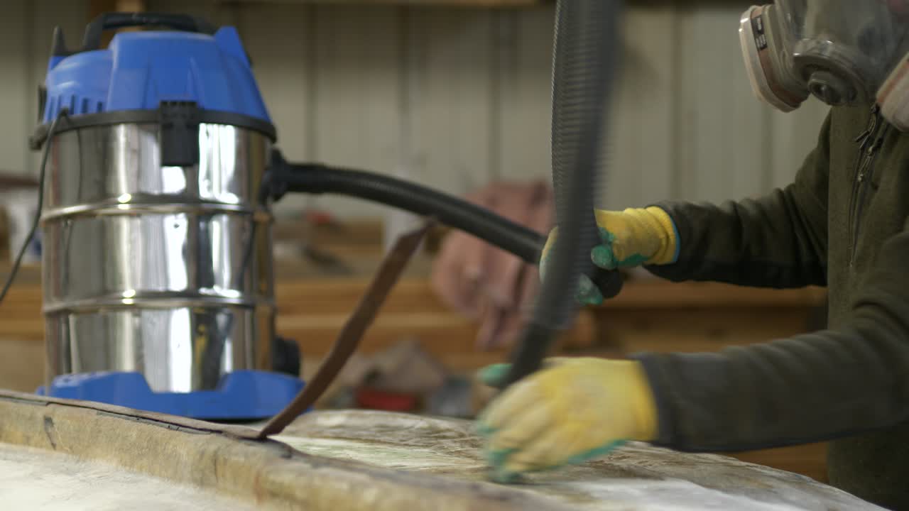 Vacuuming sanded fiberglass boat hull wearing respiratory protection