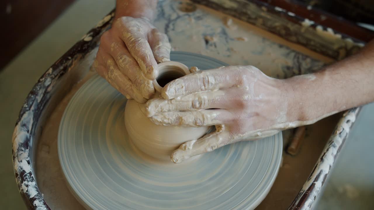 Primo piano delle mani di un uomo che modella un vaso di ceramica lavorando al tornio da vasaio in studio.