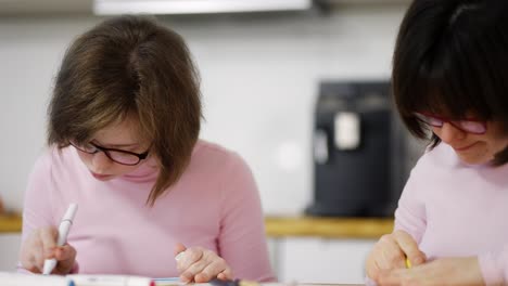 Portrait-of-two-girls-draw-with-colorful-pens-at-home,-close-up