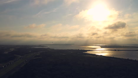 aerial view over the marsh - road facing the golden sunset as a bird investigates the drone in flight
