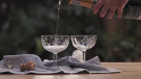 Serving-a-fancy-champagne-bottle-in-two-glass-cups-on-a-table-outdoors