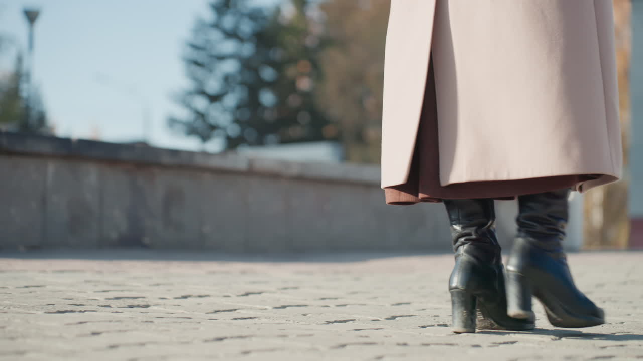 Scatto dinamico di un outfit elegante e dell'andatura. Calzature e abbigliamento chic in un luminoso ambiente urbano. Persona sicura che cammina attraverso una piazza cittadina illuminata dal sole indossando abiti e calzature alla moda.