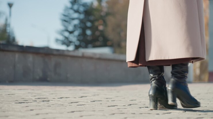 Scatto dinamico di un outfit elegante e dell'andatura. Calzature e abbigliamento chic in un luminoso ambiente urbano. Persona sicura che cammina attraverso una piazza cittadina illuminata dal sole indossando abiti e calzature alla moda.