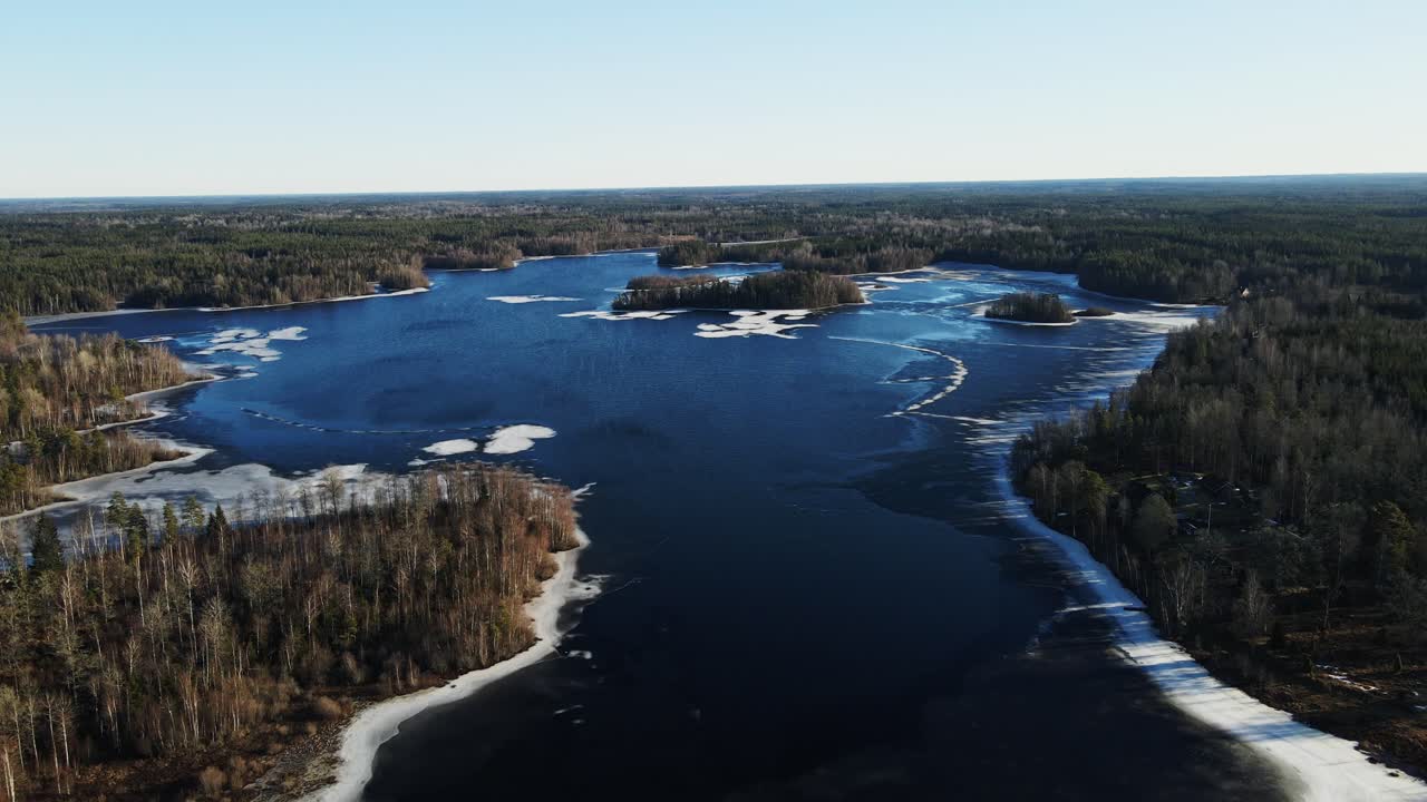 Beautiful aerial view of a frozen lake surrounded by a vast forest in rural Sweden on a sunny winter day
