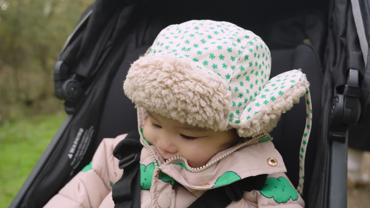 Adorable Asian baby laughs in stroller whilst wearing warm wooly hat to keep him warm during winter