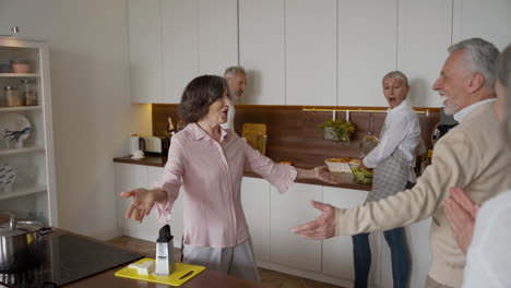 grupo de amigos sênior alegres cumprimentando uns aos outros com abraços na cozinha