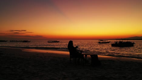young woman relaxing by the water taking photos of the beautiful orange and yellow sunset