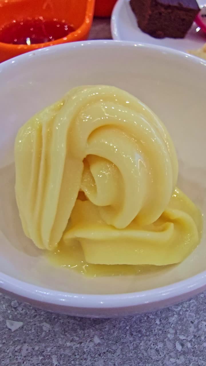 Close-up of vanilla soft serve ice cream swirled in a white bowl, placed on a table with other desserts in the background