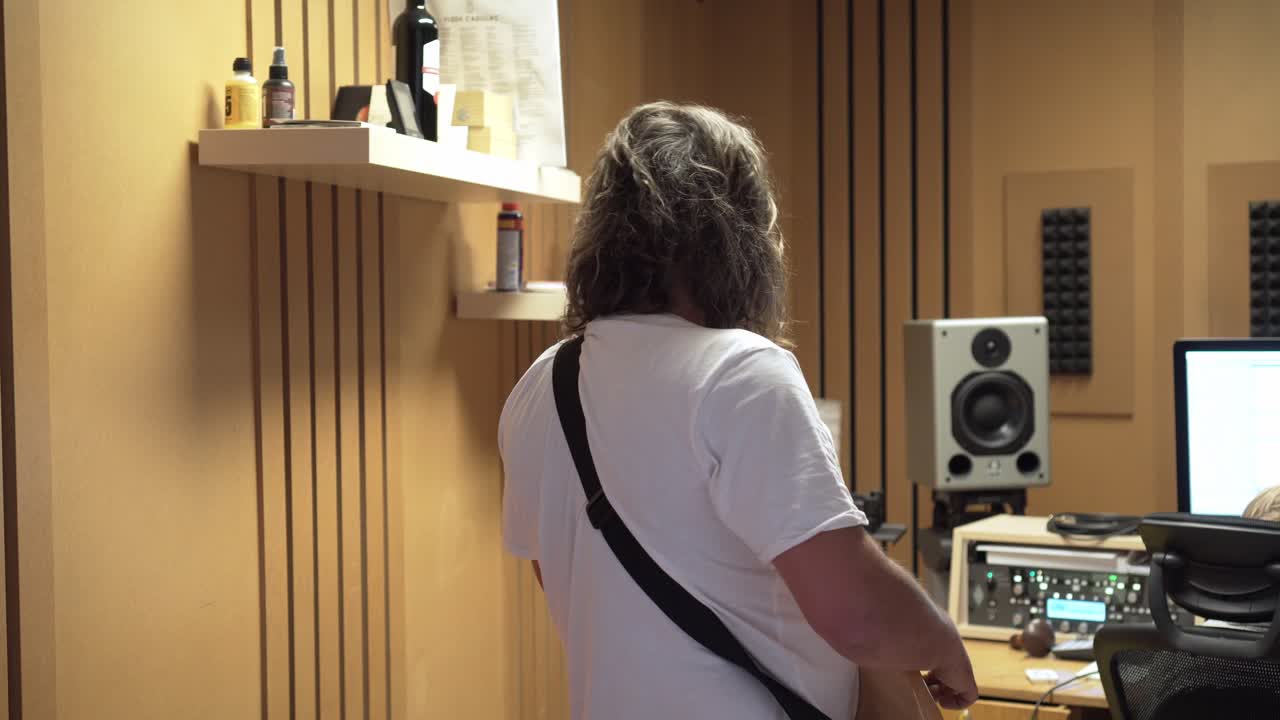 Man playing bass guitar in recording studio, back view