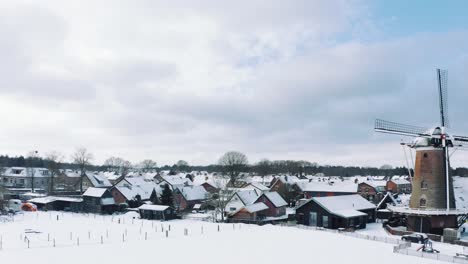 Drohnenansicht-Eines-Kleinen-Dorfes-Mit-Windmühle-In-Gardenen,-Schneebedeckter-Veluwe-Nationalpark