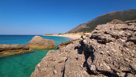 Hidden-Secret-Beach-Beckons-Behind-Rocks,-Washed-by-the-Azure-Waters-of-the-Enchanting-Ionian-Sea-in-Albania