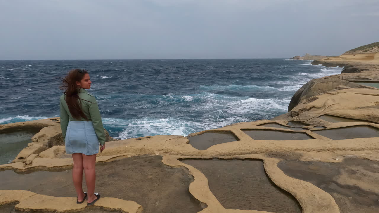 una dama se para en los acantilados de la isla de malta y mira el mar