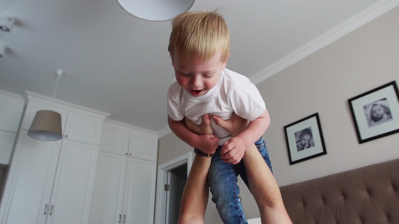 Dad keeps a dignity above himself lying on the bed. A boy in a white T-shirt laughs and smiles from playing with his father