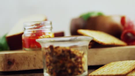 green olives, jam, pickles and crackers on wooden board