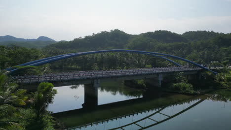 Drohne-Biegt-Flussaufwärts-Ab-Und-Fängt-Motorroller-Ein,-Der-Eine-Brücke-Im-Pantai-Soge-In-Indonesien-überquert