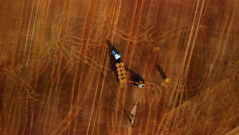 an aerial view of a large industrial golden field with a tractor collecting hay bales, top down