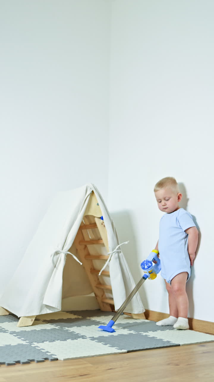 Cute boy 2 years old vacuuming at home. Toddler boy cleaning the room with a handheld vacuum cleaner. Child self-development, little helper in the housework