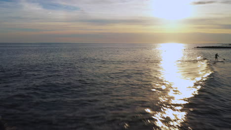 low-altitude-drone-camera-dolly-shot-forward-above-a-jetty-with-a-golden-sunset-in-view---surfers-below-waiting-for-the-perfect-wave