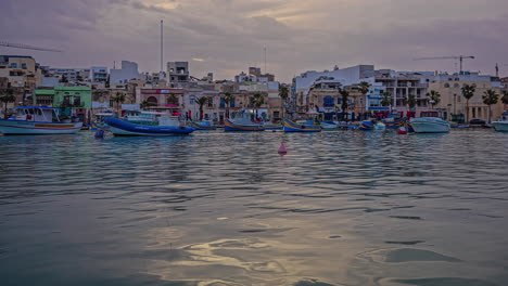 Picturesque-timelapse-shot-of-some-fishing-boats-docked-along-seaside-off-the-coast-of-Marsaxlokk,-Malta-on-a-cloudy-day