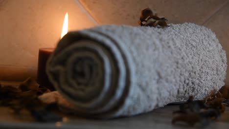 relaxing-spa-background-with-candles-with-flickering-flames,-some-wooden-petals-and-a-towel