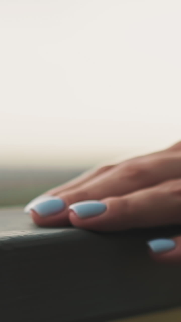 Hand of young woman with light blue nail polish runs over metal railing on city street on blurred background slow motion extreme close view