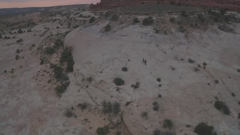 escena aérea por encima de dos personas montando sus bicicletas de montaña en roca resbaladiza a través de los vastos cañones del desierto de moab durante la puesta del sol