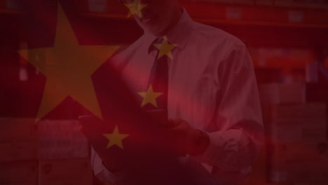 animation of chinese flag waving over man using tablet in warahouse