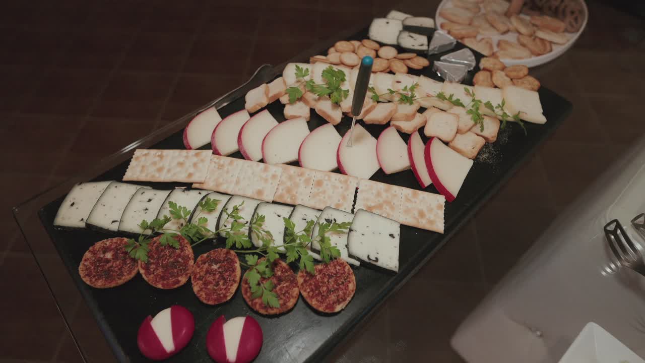 Wedding cheese board with assorted sliced cheeses, crackers, and herbs on elegant black tray
