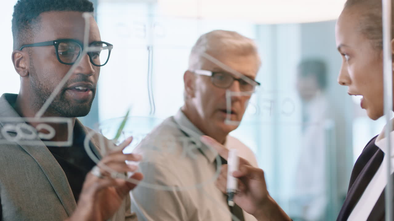 비즈니스 팀 회의는 유리 화이트보드에 붙는 메모를 사용하여 글을 쓰고 문제 해결 전략을 고민하는 동료들이 유리를 통해 사무실에서 프로젝트에 대한 해결책을 생각합니다.