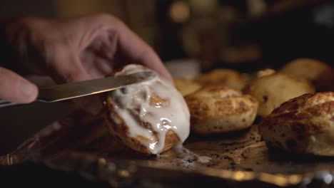 spreading the sweet sticky icing over a freshly baked cinnamon roll using a bread knife - closeup shot