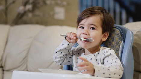 a two-year-old baby eats porridge on his own, sits in a feeding chair