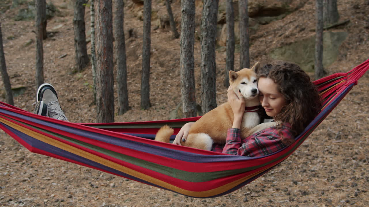 Woman relaxing in hammock with dog in forest
