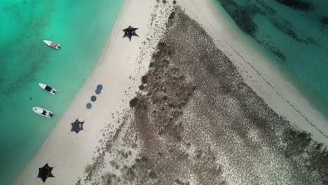 Boats-and-umbrellas-on-a-sandy-beach-with-turquoise-waters-and-a-grassy-dune,-aerial-view