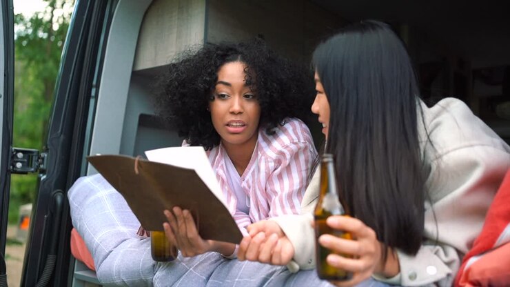 Amiche felici e diverse leggono una mappa con della birra in un camper.