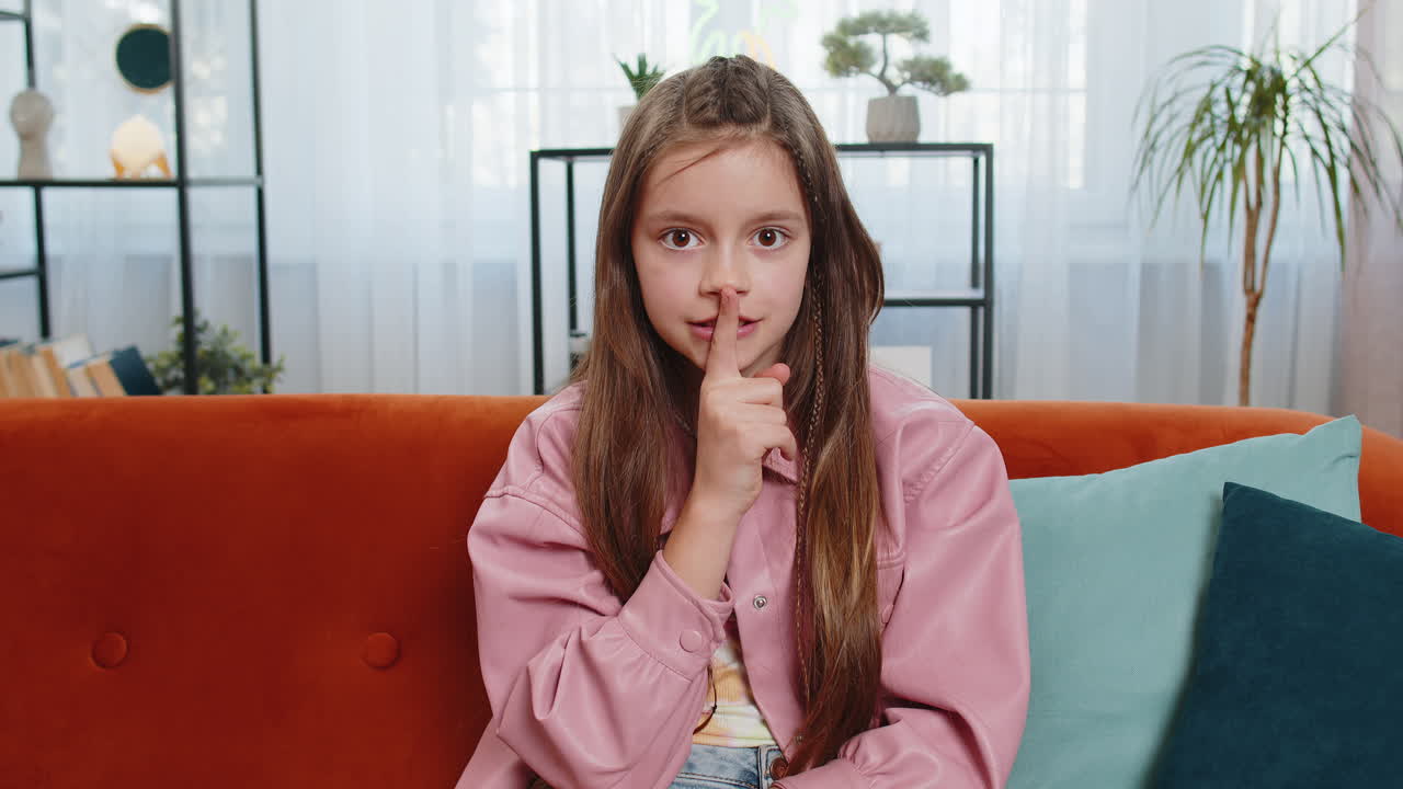 Girl child presses index finger to lips makes silence hush gesture sign do not tells gossip secret