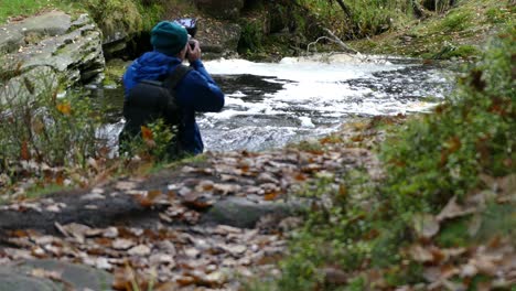 un niño pequeño, equipado con una cámara y un trípode, fotografía el pacífico bosque de otoño e invierno y su serpenteante arroyo