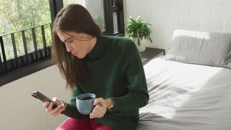 Caucasian-non-binary-transgender-woman-sitting-on-bed-and-using-smartphone