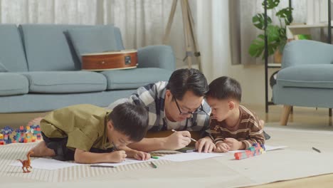 아시안 아버지와 아들의 몸이 가득 차 있고, 플라스틱 장난감 벽돌이 있는 방에서 바닥에 누워서 집에서 함께 그림을 그리고, 이야기하고, 놀고 있다.
